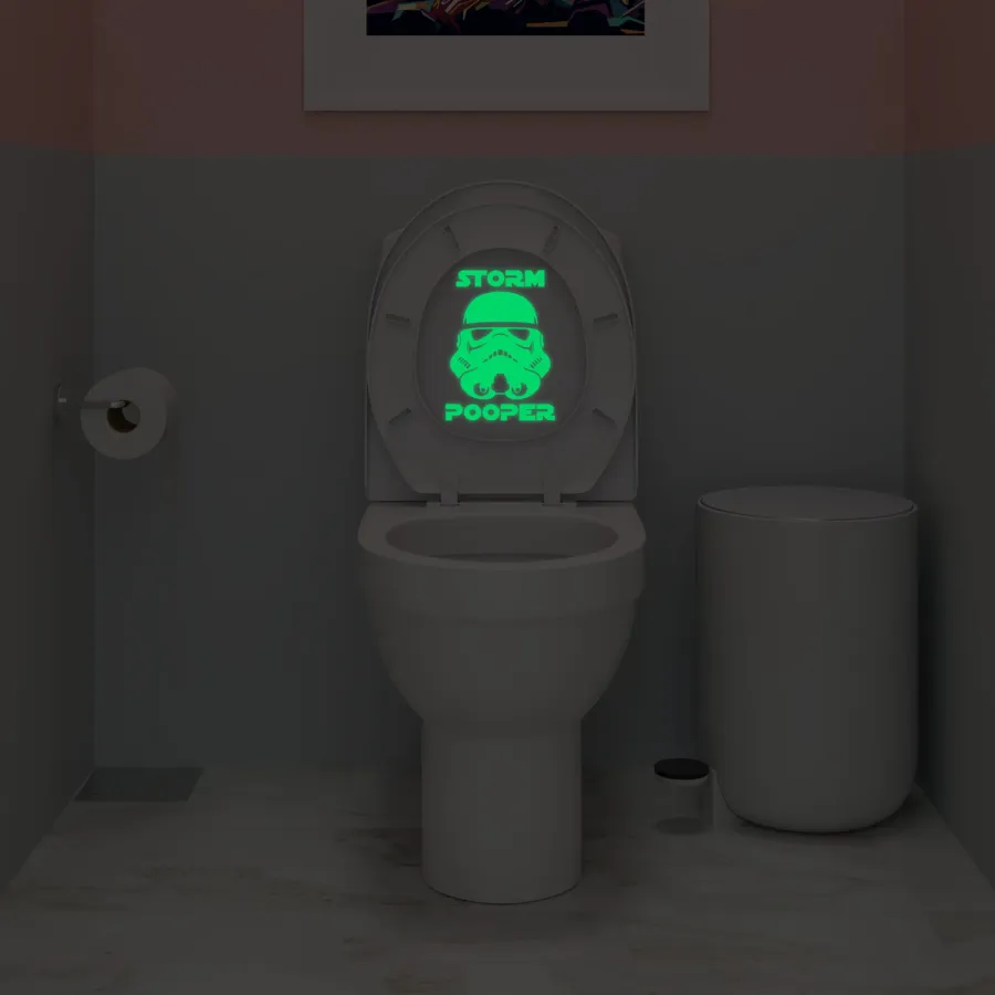 Glowing green Storm Pooper Stormtrooper helmet decal on a toilet lid in a dark bathroom